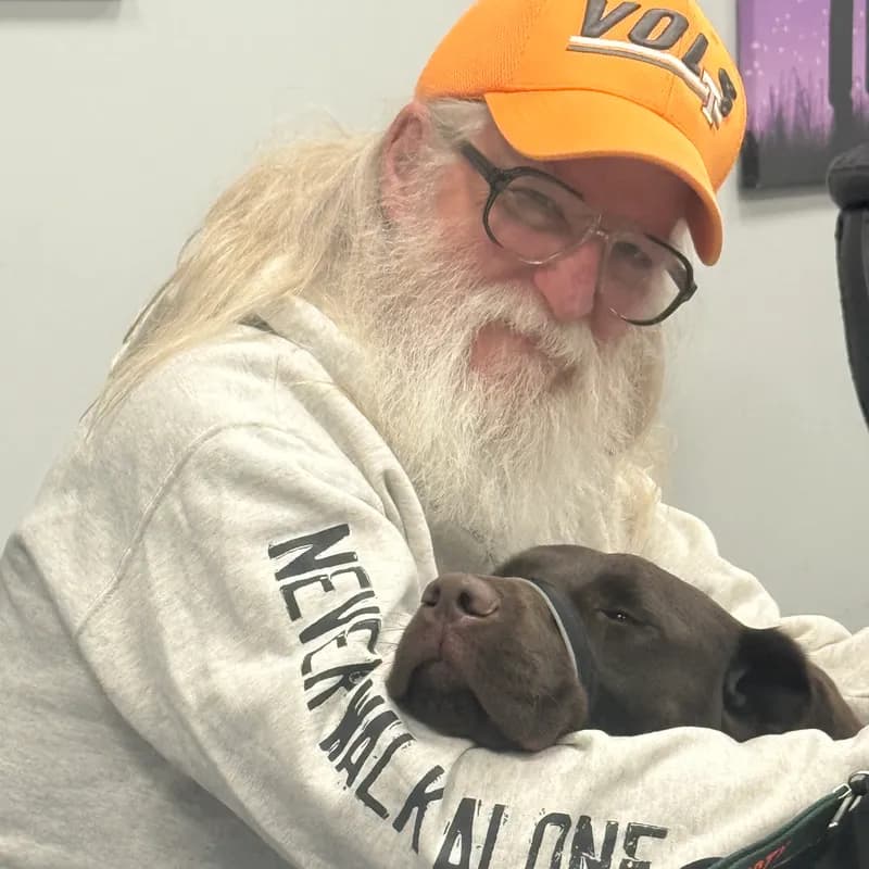 Veteran in a Never Walk Alone sweatshirt holding a sleeping chocolate Labrador service dog