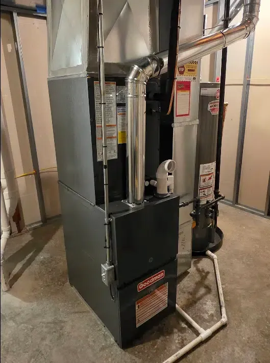 Goodman gas furnace installed in a residential basement with metal ductwork and PVC drain piping.