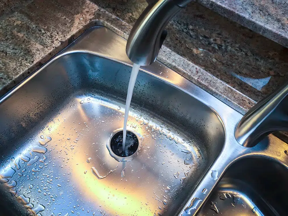 Stainless steel kitchen sink with running water from brushed nickel faucet, professional plumbing installation by Embrich Plumbing