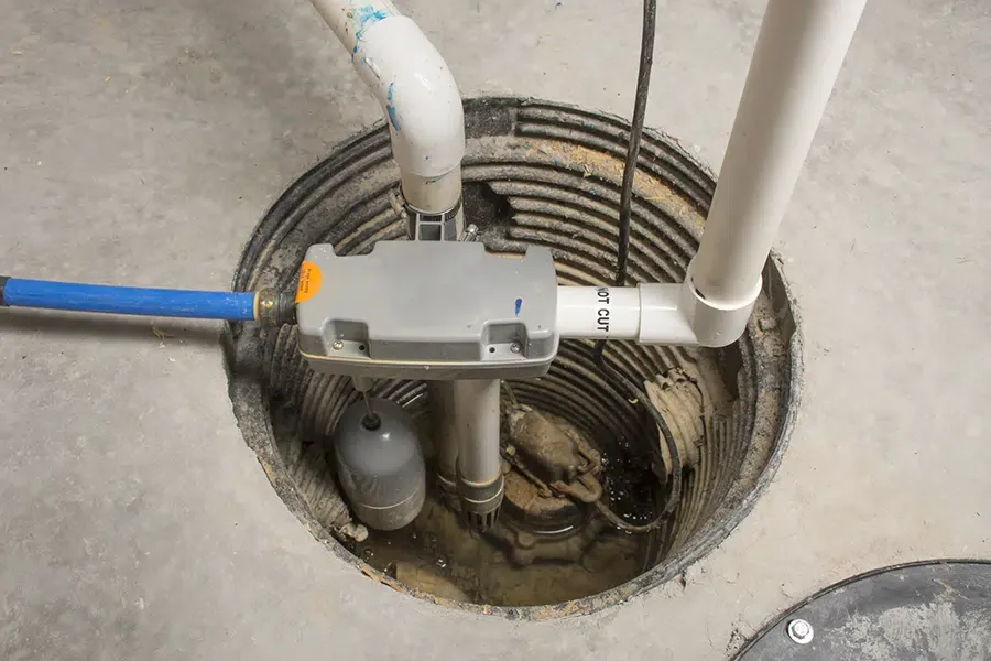 Sump pump installed in basement pit with PVC discharge pipes and float switch, serviced and installed by Embrich Plumbing