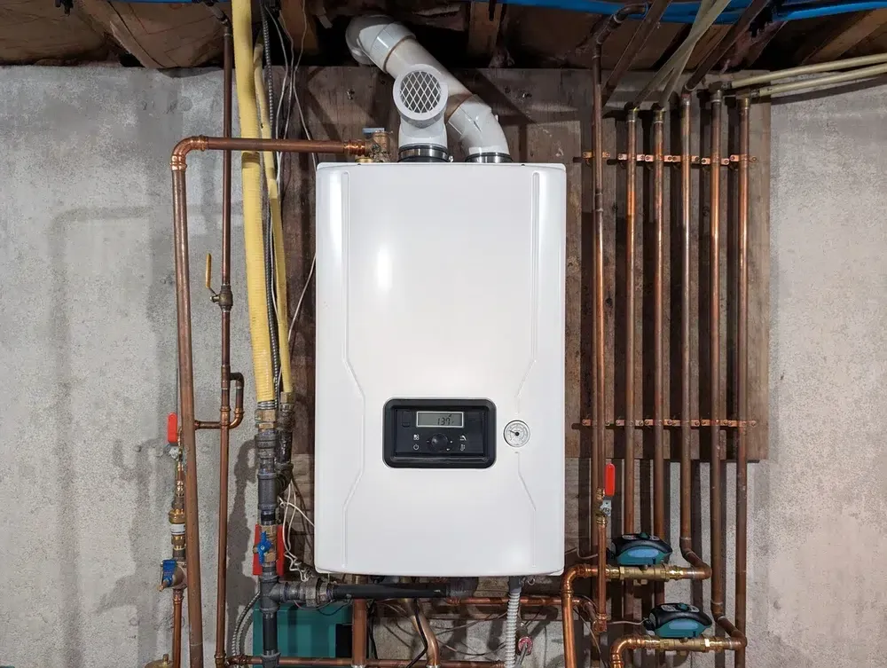 Tankless water heater installed on basement wall with copper pipe connections and exhaust vent, professionally installed by Embrich Plumbing
