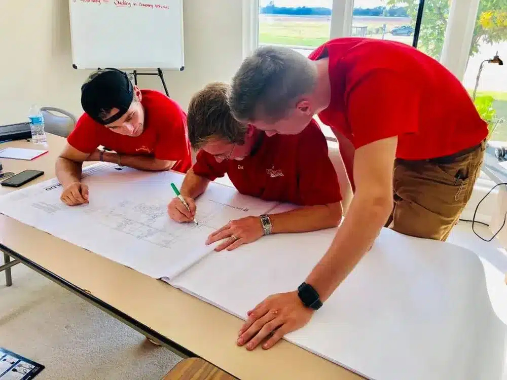 Embrich Plumbing, Heating & Air Conditioning team members reviewing plans and marking measurements on board