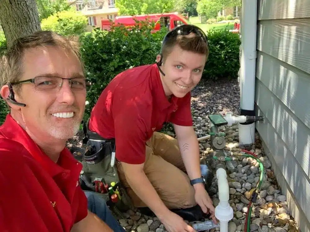Embrich Plumbing, Heating & Air Conditioning technician working on outdoor plumbing system near home foundation