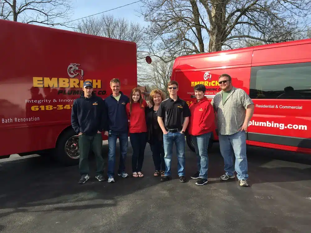 Embrich Plumbing, Heating & Air Conditioning crew standing in front of branded service trucks outside company building